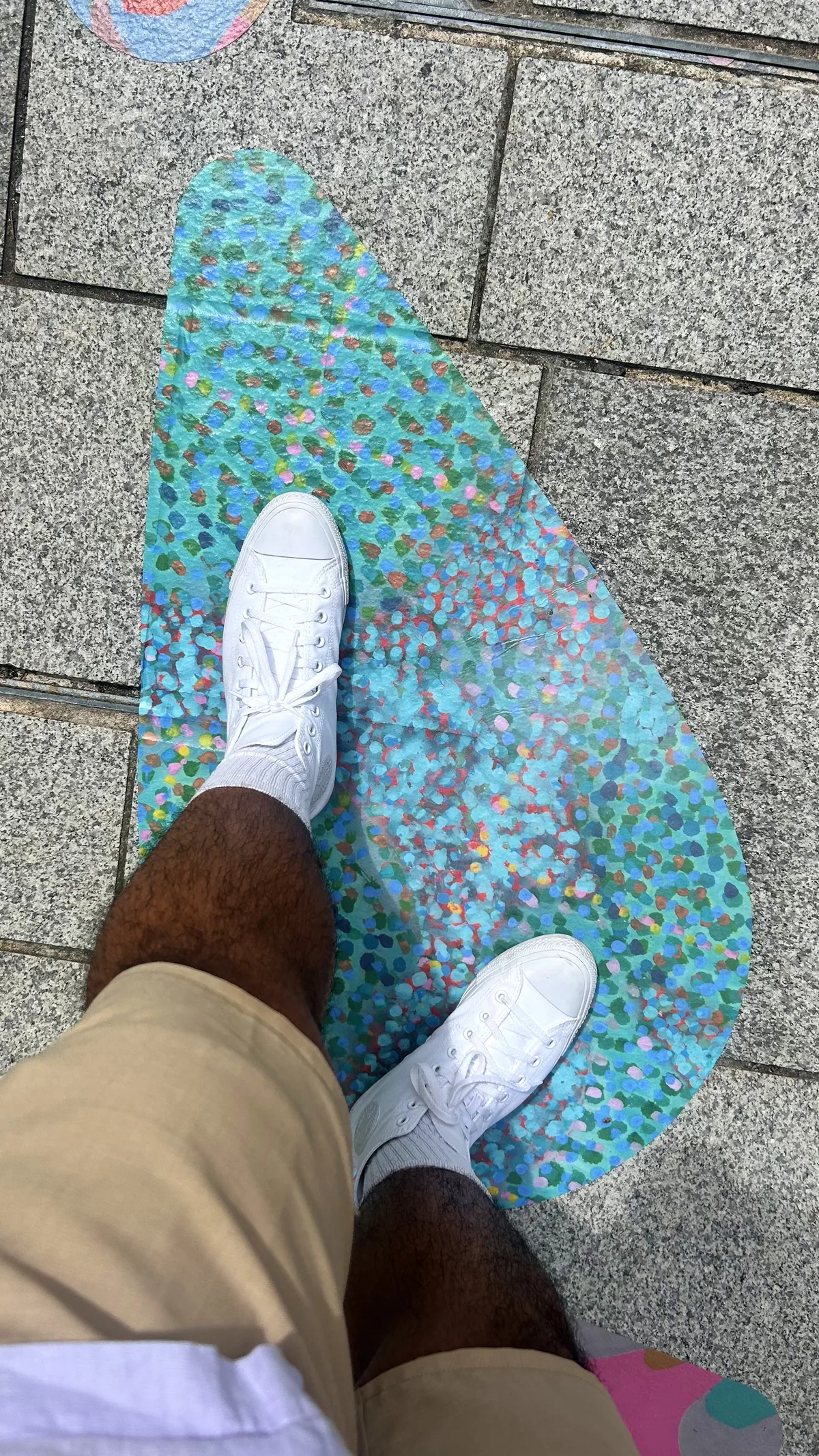 A teal teardrop decal painted in many small dots, laid on grey granite with a person's white trainers standing on it